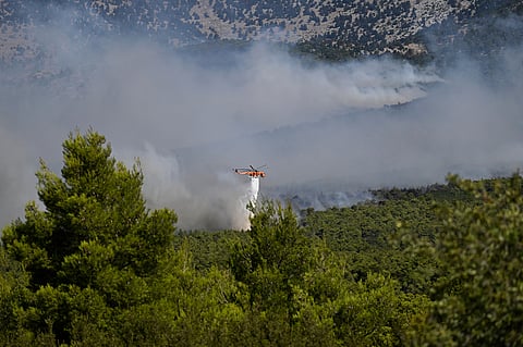 A firefighting helicopter drops water over a smoke-filled forest during a wildfire near Porto Germeno, northwest of Athens, Greece, Sunday, Aug. 2, 2026.