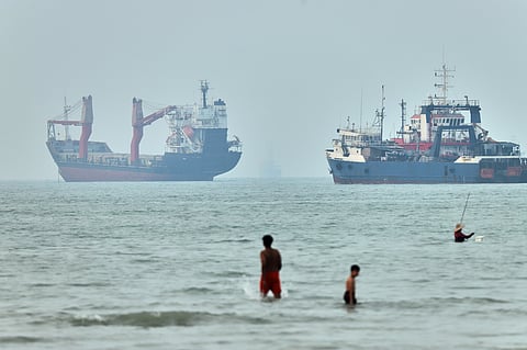 Children wade in the water with cargo ships at anchor in the background and a fisherman nearby, in the Strait of Hormuz off Bandar Abbas, Iran.