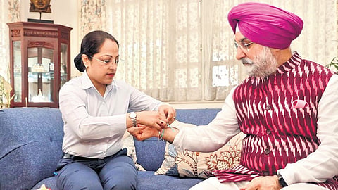A woman from Sandhu’s security team ties a rakhi to him.