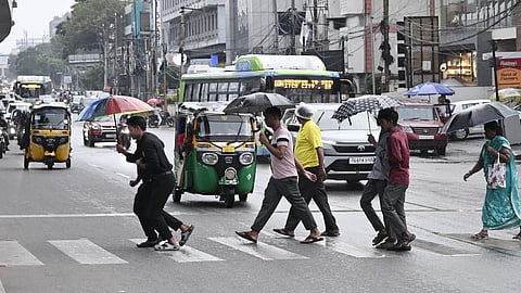 Pedestrians make their way across a zebra crossing with umbrellas during a drizzle at Rasoolpura Junction in Hyderabad on Sunday.