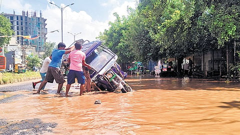 An e-rickshaw plunged into a waterlogged, pothole-ridden street in Gurugram last year as pedestrians wade through flooded stretch to help the driver.