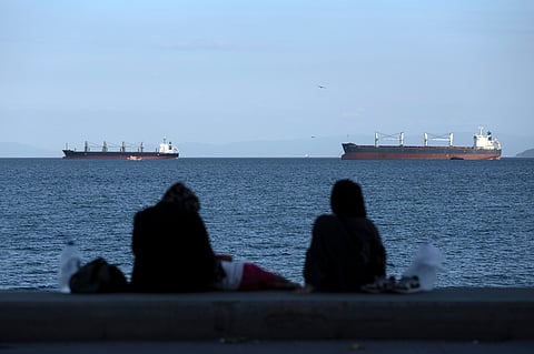 People sit in front of cargo ships anchor in the Marmara Sea await to cross the Bosphorus Straits in Istanbul, Turkey, on July 13, 2022.