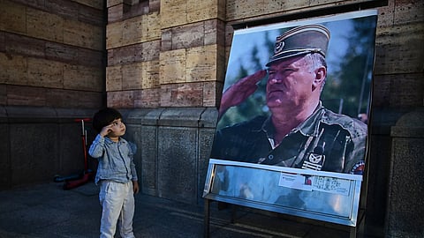 A boy salutes in front of a poster of former Bosnian Serb wartime general Ratko Mladic, outside a church in Banja Luka, Bosnia-Herzegovina, Thursday, Aug. 27, 2026.