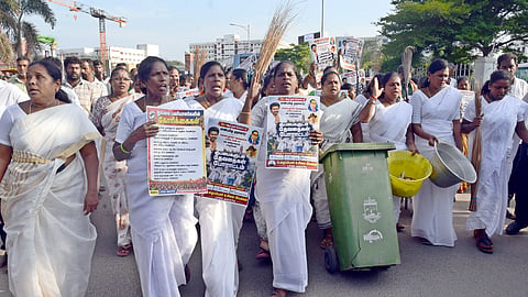 Sanitary workers continued their protest on the 14th day on Wednesday near Ripon Building, with several of them dressed in white and carrying garbage to mock minister Rajmohan’s remark that they are “sanitary angels”.