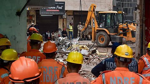 National Disaster Response Force (NDRF) personnel watch as an excavator clears debris during search and rescue operations, a day after a five-storey building housing a boys' hostel collapsed, at Satya Niketan, in New Delhi, Monday, Sept. 7, 2026.
