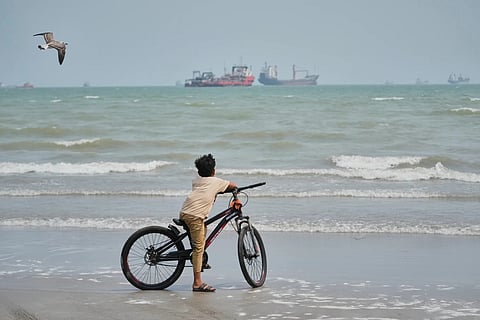 A gull flies overhead as a boy stands with his bicycle on a beach overlooking commercial vessels anchored in the Strait of Hormuz off Bandar Abbas, Iran on Monday
