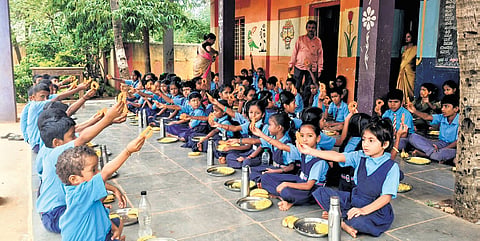 Students hold up sweets served to them as part of the Amrut Bhojan project at a 
government school in Gadag. 