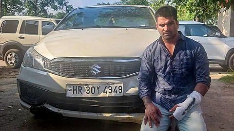 Accused Kalyan Bainsla kneels beside his vehicle in police custody following his arrest in connection with a hit-and-run case involving a woman biker, in Gurugram, Haryana, Tuesday, Sept. 15, 2026.