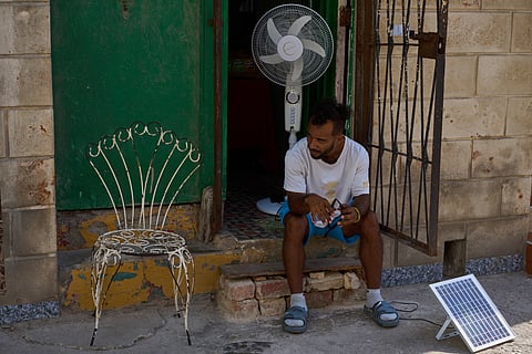 A man charges his fan's battery at his doorway using a small solar panel set up on the street during a blackout in Havana, Cuba, Friday, Sept. 18, 2026