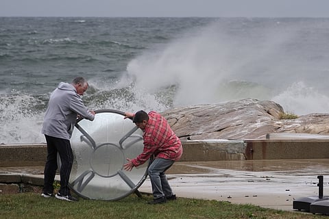 People move an outdoor table away from the shorefront during the early stages of a nor'easter storm, Friday, Sept. 25, 2026, in Gloucester, Mass.