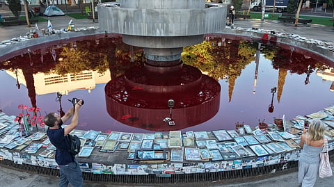 People take pictures of the Dizengoff Fountain, filled with red dye in the Israeli coastal city of Tel Aviv on October 7, 2026, to mark the third anniversary of Hamas's October 7 attack.