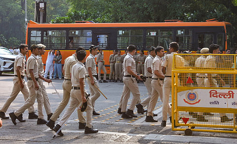 Delhi Police personnel walk past barricades near a bus during a deployment at Mandi House Circle, in New Delhi on Monday.