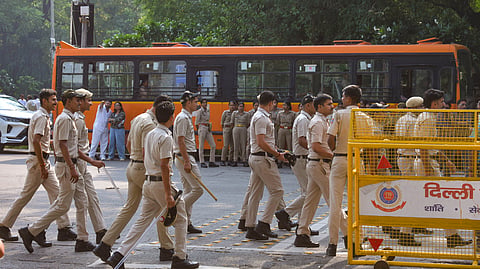 Delhi Police personnel walk past barricades near a bus during a deployment at Mandi House Circle, in New Delhi on Monday.