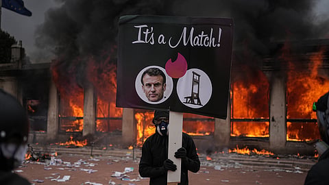 A protester holds a board with a photo of French president Emmanuel Macron in front of a burning tourism office during a demonstration against rising living costs and in solidarity with students' grievances in Lyon, France, Saturday, Oct. 17, 2026.