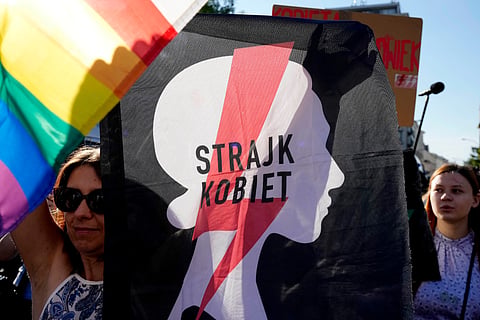  A woman with the sign of a women's rights organization and with a pro-LGBT+ rights flag take part in a protest in Warsaw, Poland, Tuesday, July 23, 2024.