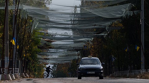 A local man rides a bicycle beneath anti-drone nets stretched over a street during a local ceasefire related to a humanitarian aid mission in Oleshky, in Kherson, Ukraine, Wednesday, Oct. 28, 2026.