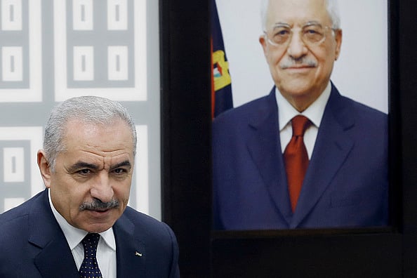 Getty Images : Palestinian Prime Minister Mohammad Shtayyeh stands next to a portrait of the Palestinian Authority's President Mahmud Abbas during a cabinet meeting |