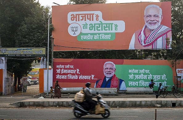 Getty Images : A motorcyclist travels past campaign banners for the BJP featuring PM Modi in Patna, Bihar.