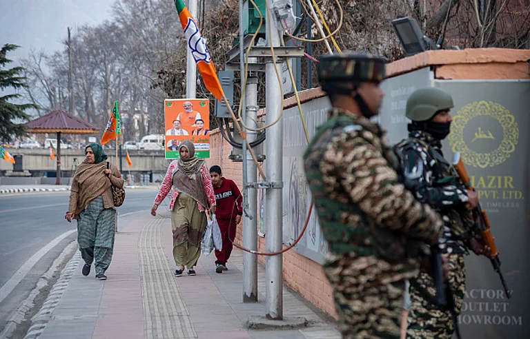 Women walk along a street adorned with Bharatiya Janata Party (BJP) flags and boards, while Indian paramilitary troopers stand alert ahead of Prime Minister Narendra Modi's visit. - (Photo by Idrees Abbas via Getty Images)