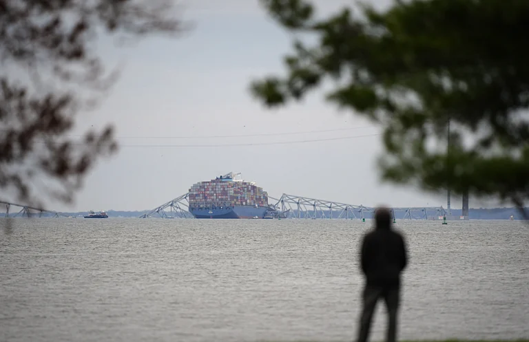 A person views from Fort McHenry a container ship as it rests against the wreckage of the Francis Scott Key Bridge. - AP