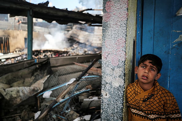 Majdi Fathi/NurPhoto via Getty Images) : A Palestinian boy is inspecting the site of an Israeli strike on a school sheltering displaced people