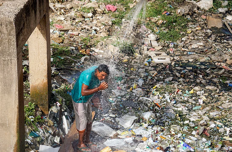 A man bathes with water leaking from a pipeline at Nizamuddin area on a hot summer day, in New Delhi - PTI