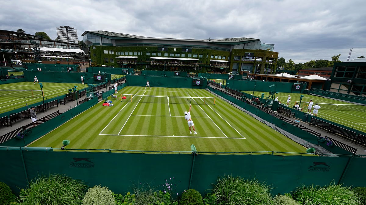 Tennis players train as a member of ground staff waters the plants at the All England Lawn Tennis and Croquet Club in Wimbledon, London, Friday, June 28, 2024. The Wimbledon Championships begin on July 1.  - (AP Photo/Kirsty Wigglesworth)