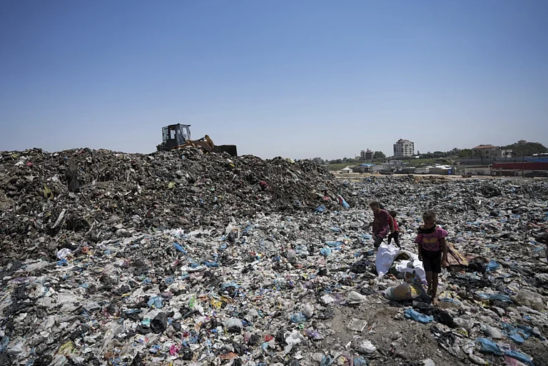 Children in sandals trudge through water contaminated with sewage and scale growing mounds of garbage in Gaza's crowded tent camps for displaced families | - AP