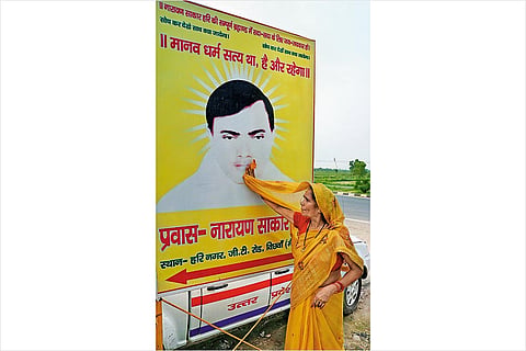 A devotee from Agra wipes a poster sporting a photo of Baba Bhole Nath outside his ashram in Mainpuri, UP