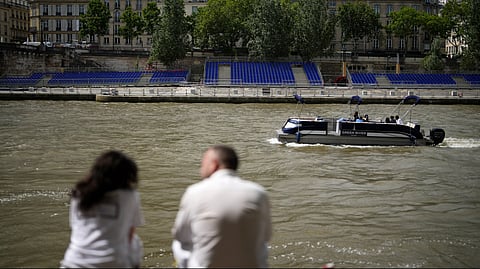 People sit along the Seine river with stands installed on its banks, Thursday, July 4, 2024 in Paris. The Seine river will host the Paris Olympic Games opening ceremony on July 26.