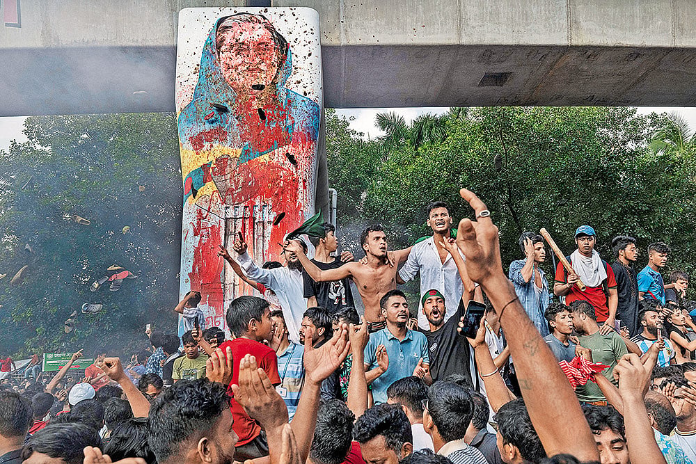 Protesters celebrate beside a defaced portrait of Hasina in Dhaka on August 5, 2024