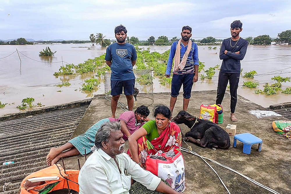 People wait on the roof of a house for evacuation from a flood-affected area in Vijayawada