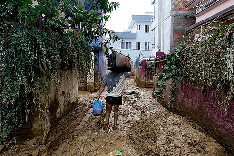 Nepal Floods: A man walks on a muddy alleyway carrying belongings salvaged from his house