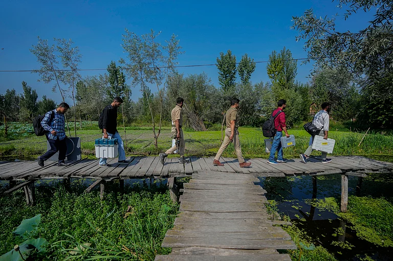 Polling officials and police walk on a wooden bridge towards a polling station in the interior of Dal Lake - Associated Press