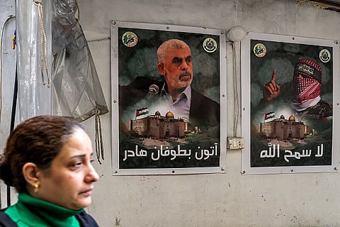 A woman walks past posters depicting Yahya Sinwar (L) and Abu Obeida (R), the masked spokesman of the Qassam Brigades (Hamas' armed wing), in Beirut's southern suburb on February 5, 2024 |