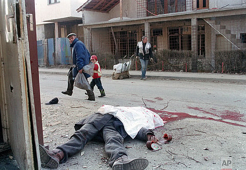 A father and his son pass the dead body of a Bosnian policeman killed when a shell landed next to his guard house in Sarajevo, Bosnia and Herzegovina, Dec. 30, 1992 |