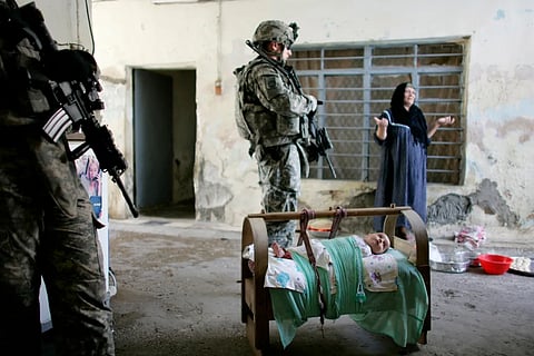 An Iraqi baby lies in a cradle while a woman argues with US soldiers searching for weapons, explosives and information about militants in the area during a foot patrol in neighbourhoods of Mosul, June 26, 2008 |