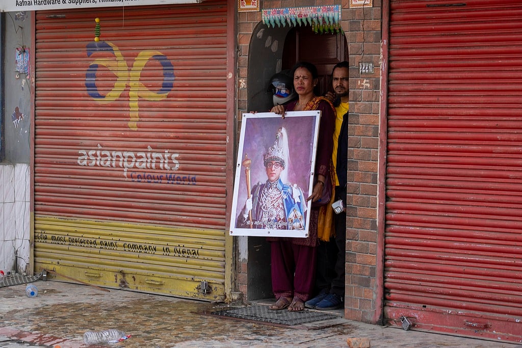 | Photo: AP : A pro-monarchist supporter carrying former late king Mahendra Shah photo take cover during a protest in Kathmandu, Nepal, on Friday, March 28, 2025. 