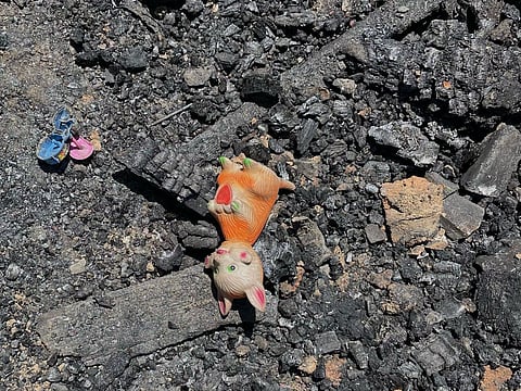 Burnt toys, charred notebooks, and blackened beams lie scattered in the rubble |
