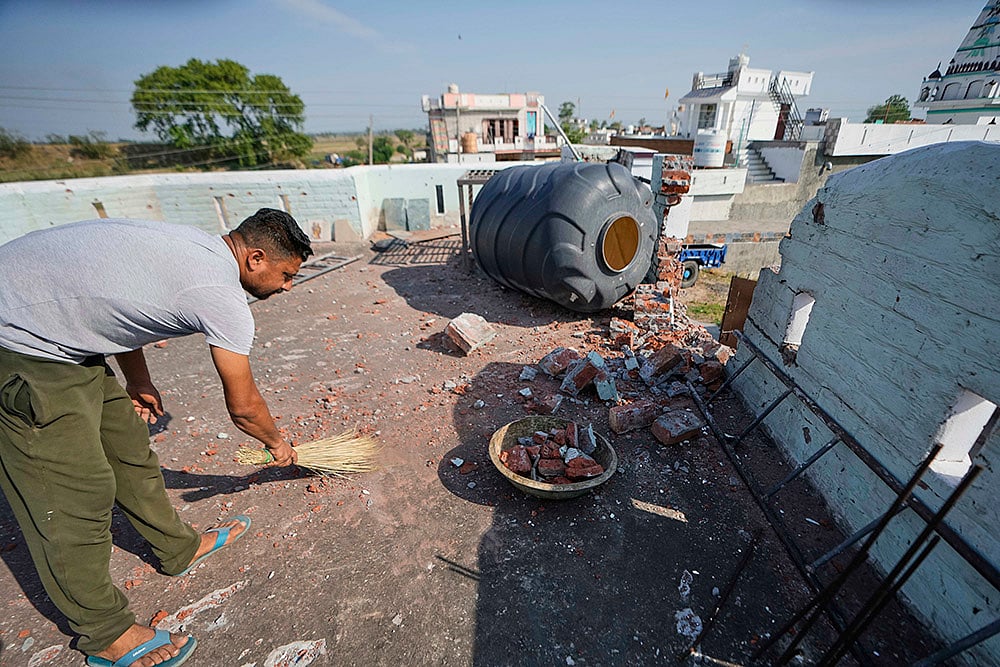 A villager cleans the roof of his house damaged by Pakistani artillery shelling at RS Pura