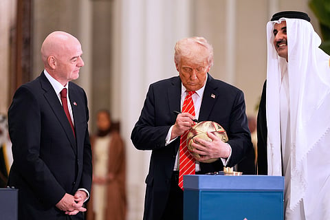 USA President Donald Trump signs a ball as Qatar's Emir Sheikh Tamim bin Hamad Al Thani and FIFA President Gianni Infantino look on at the Lusail Palace in Doha, Qatar on May 14, 2025. It marked the passing of World Cup hosting rights from Qatar to the United States.