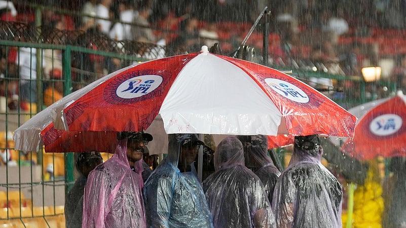 Security personnel shelter from the rain under an umbrella shortly before IPL 2025 restart