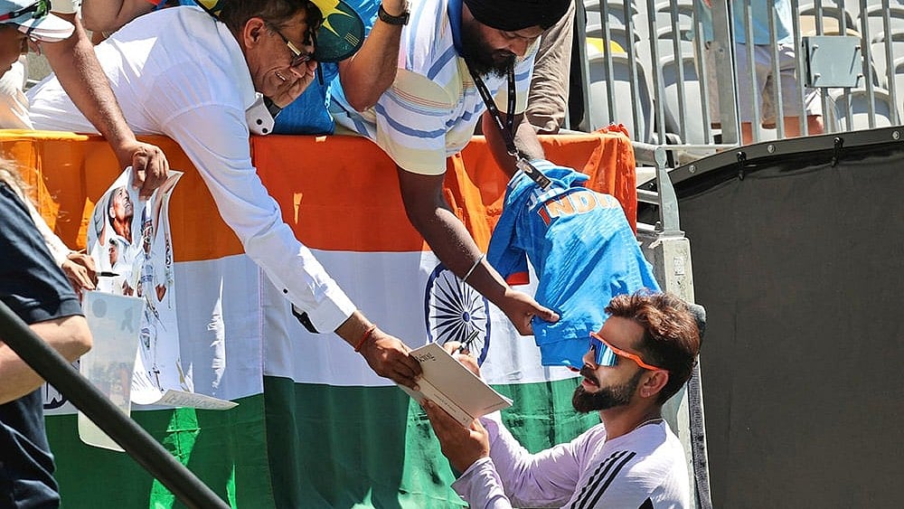 File :  India's Virat Kohli autographs a book for a fan.