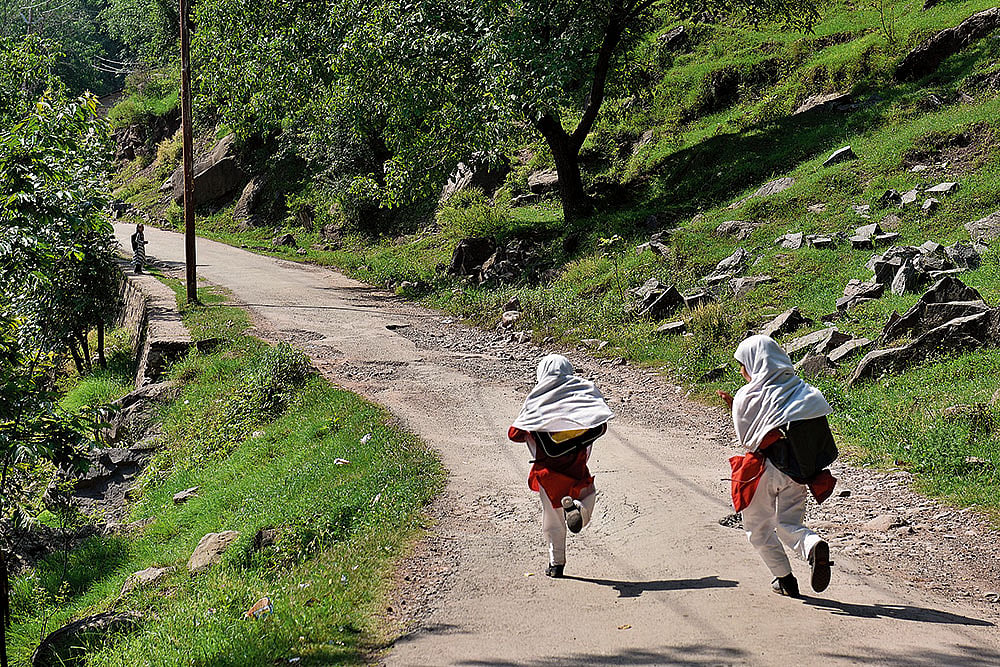 Two school girls rush back home. A security personnel is seen guarding the road