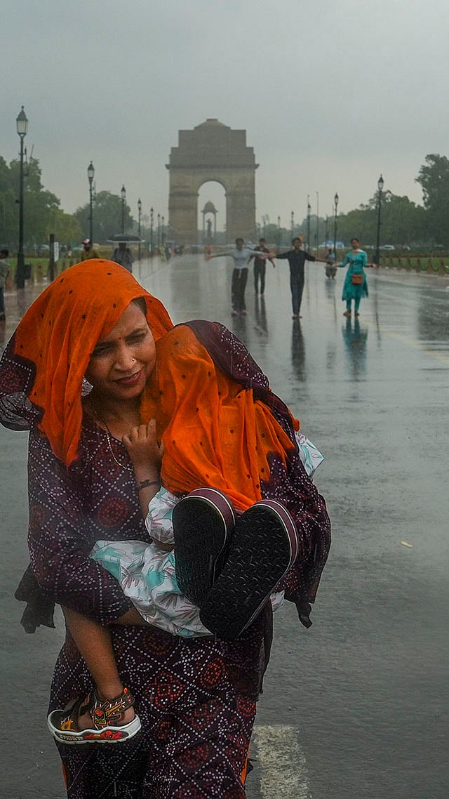 A woman covers her child with a scarf during rain, at Kartavya Path, in New Delhi. - | Photo: PTI/Manvender Vashist Lav