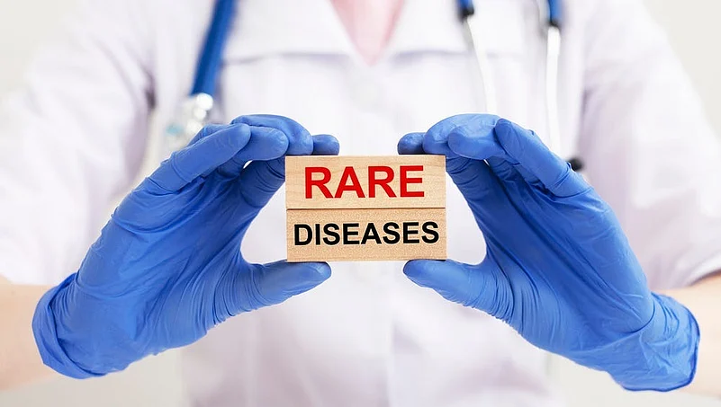 A medical worker wearing gloves holding a wooden sign reading Rare Diseases