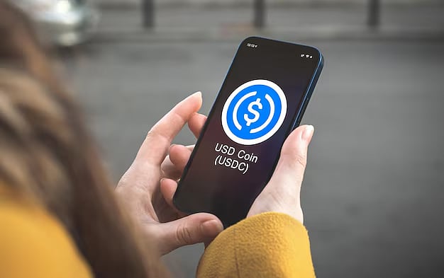 A woman holding a phone with USD coin logo