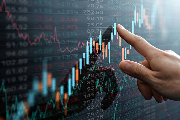 A hand points to a digital financial chart with glowing blue and orange lines.