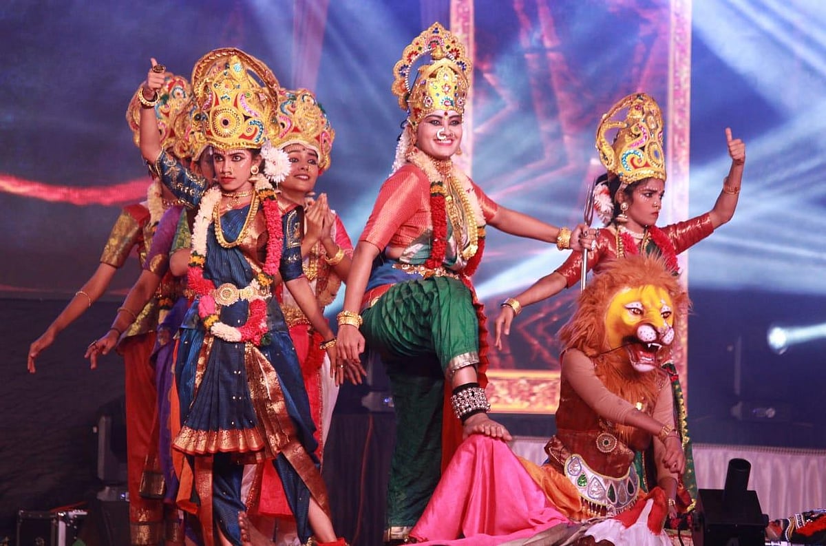 A group of performers in elaborate costumes and headdresses on a lit stage