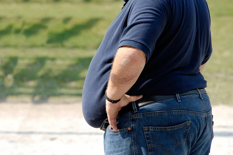 Close-up of an overweight man in a navy shirt and jeans standing outdoors with hands on waist